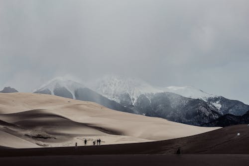 People on Wasteland Walking Towards Dune