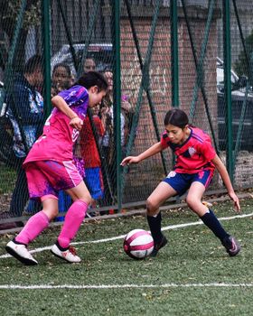 Two young girls compete passionately during a vibrant youth soccer game outdoors.