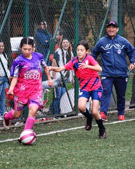 Two young girls playing football under the guidance of an encouraging coach in a lively outdoor match.