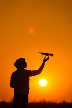 Silhouette of a man launching a drone during sunset under a dramatic sky.