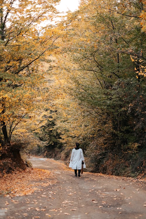 Person Wearing a White Coat Walking on Unpaved Pathway