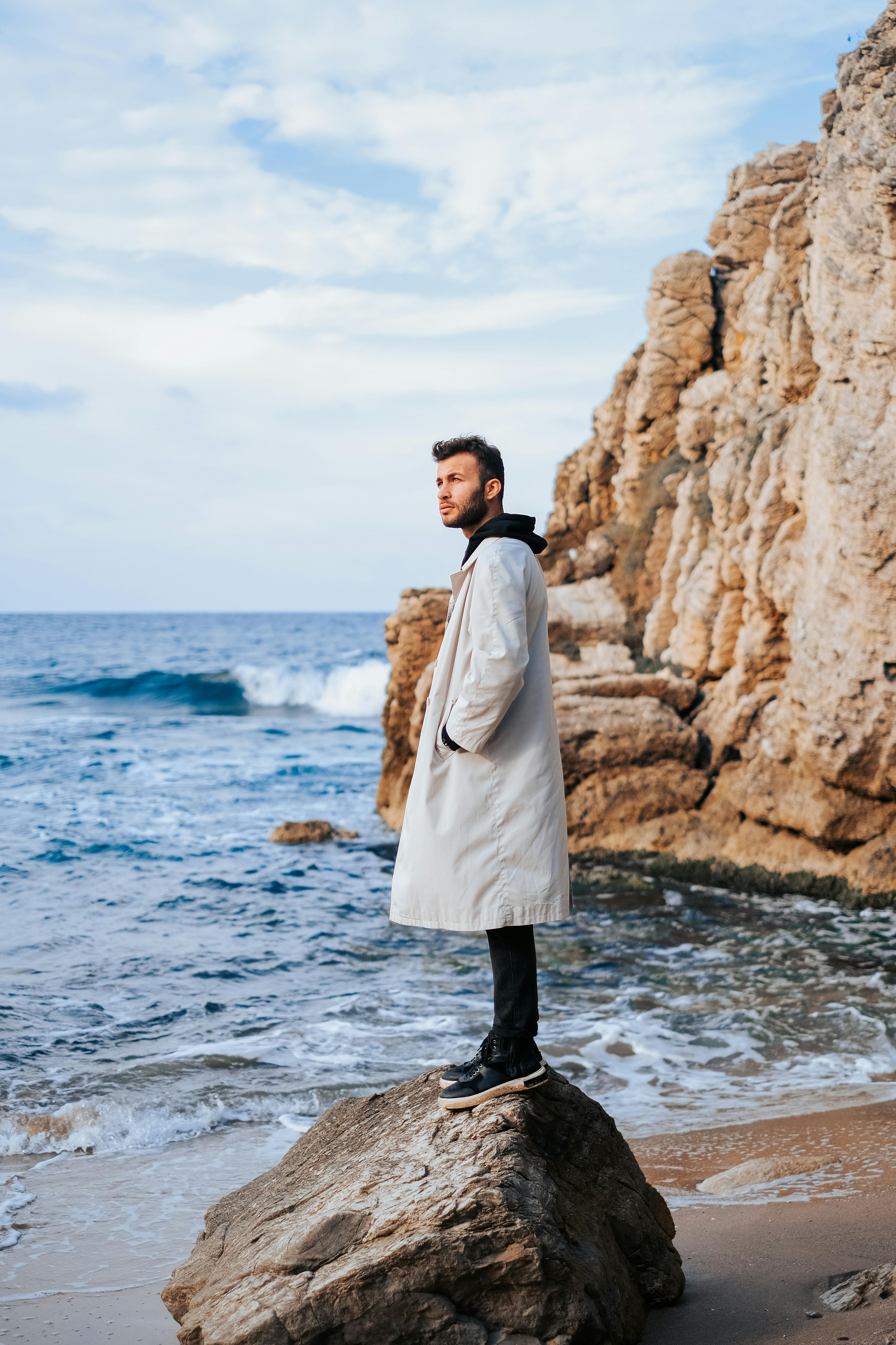 一个时尚的男人在岩石海滩上穿着外套，将时尚与自然之美融合在一起