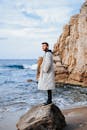 一个时尚的男人在岩石海滩上穿着外套，将时尚与自然之美融合在一起