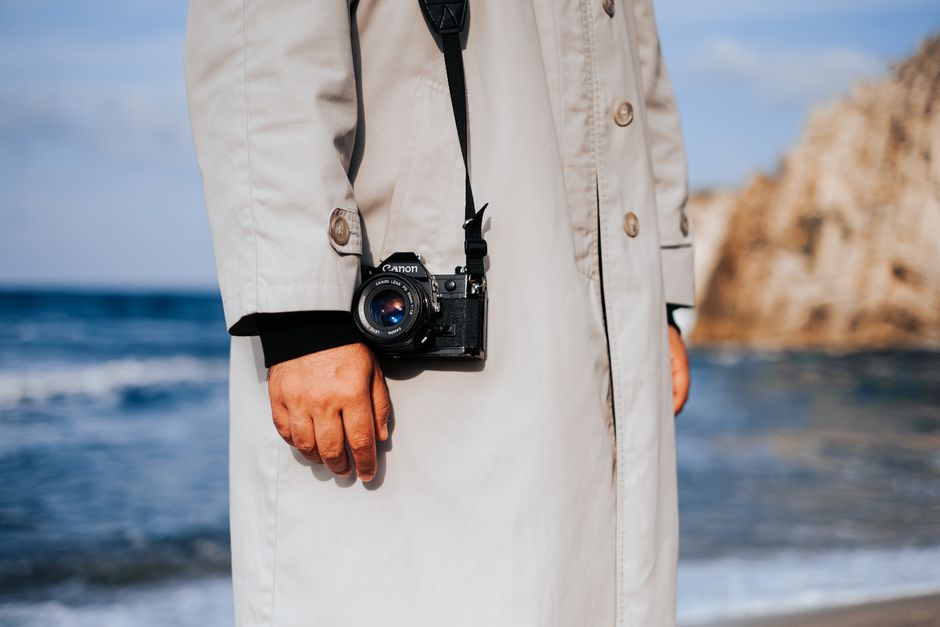 Close-up of person with camera on beach in a trench coat.