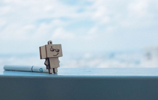 A wooden robot figurine stands charmingly on a ledge with a cloudy sky backdrop.