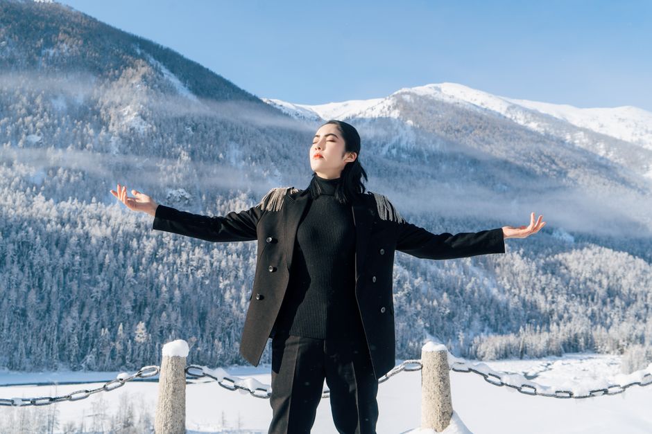 Woman in black outfit meditating amidst snowy mountains under a clear winter sky.