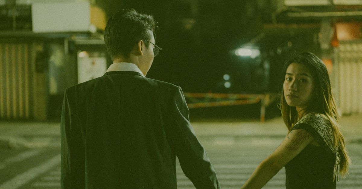 A couple holding hands while crossing a city street at night under urban lights.