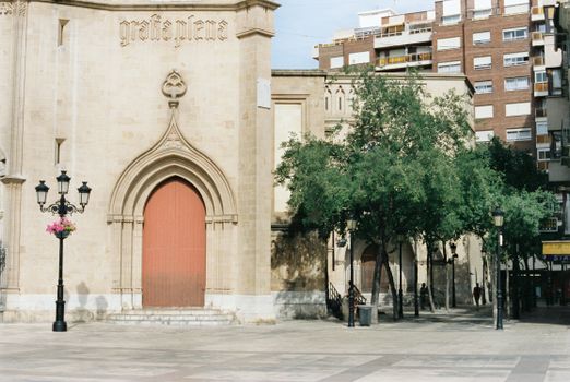 A detailed view of a church facade with gothic elements in a town square surrounded by buildings and trees.