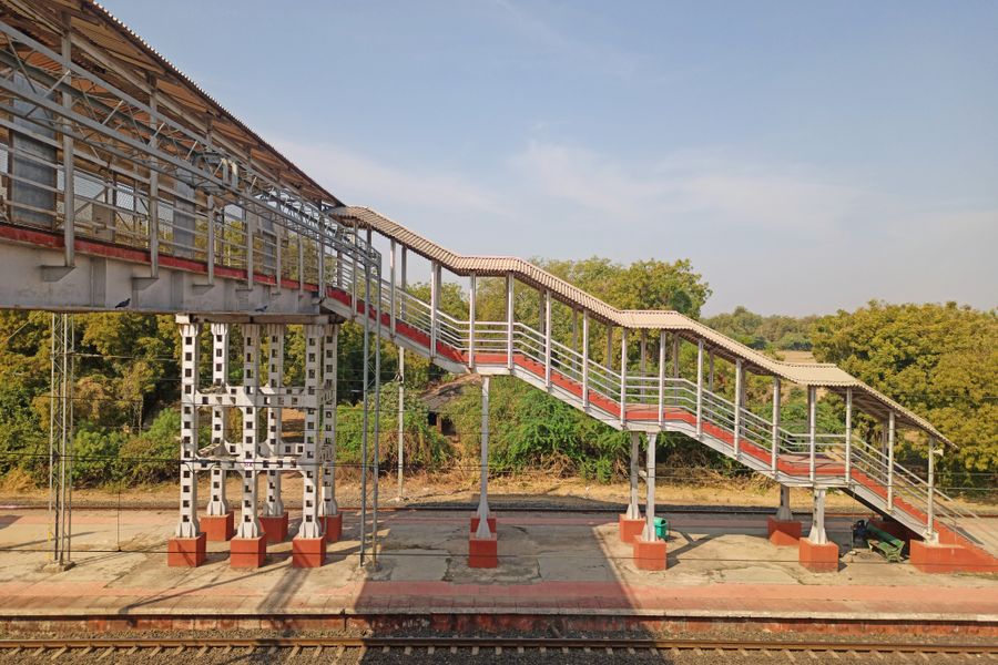 Footbridge over railway tracks at an Indian station with clear skies.