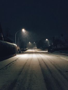 A tranquil snow-covered road illuminated by streetlights during a winter night.