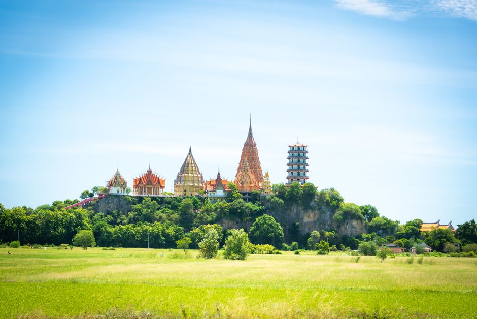 Vergulde Thaise tempel op een heuvel boven groene rijstvelden onder een blauwe lucht