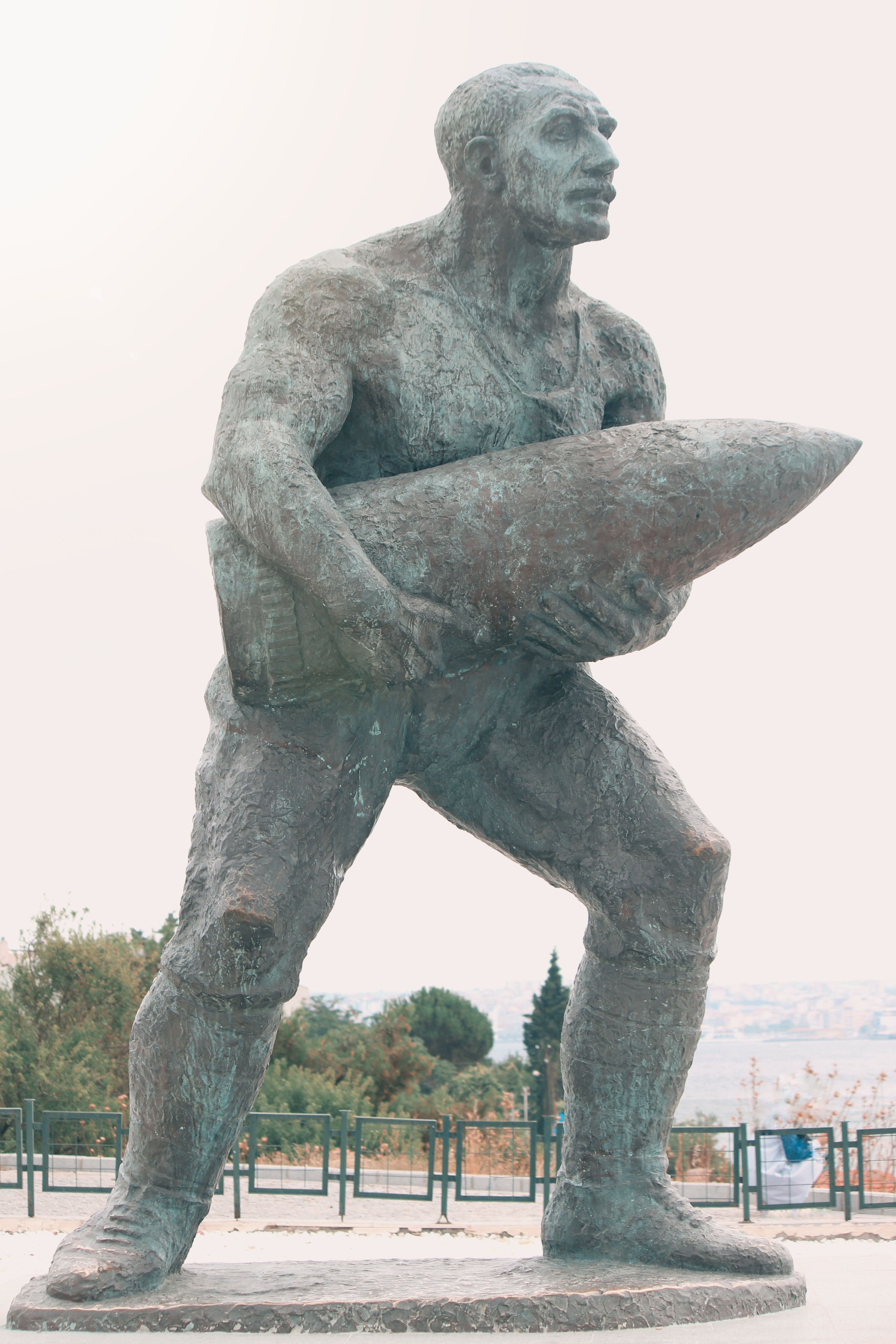 Statue of a soldier holding a large artillery shell, symbolizing strength and military history.