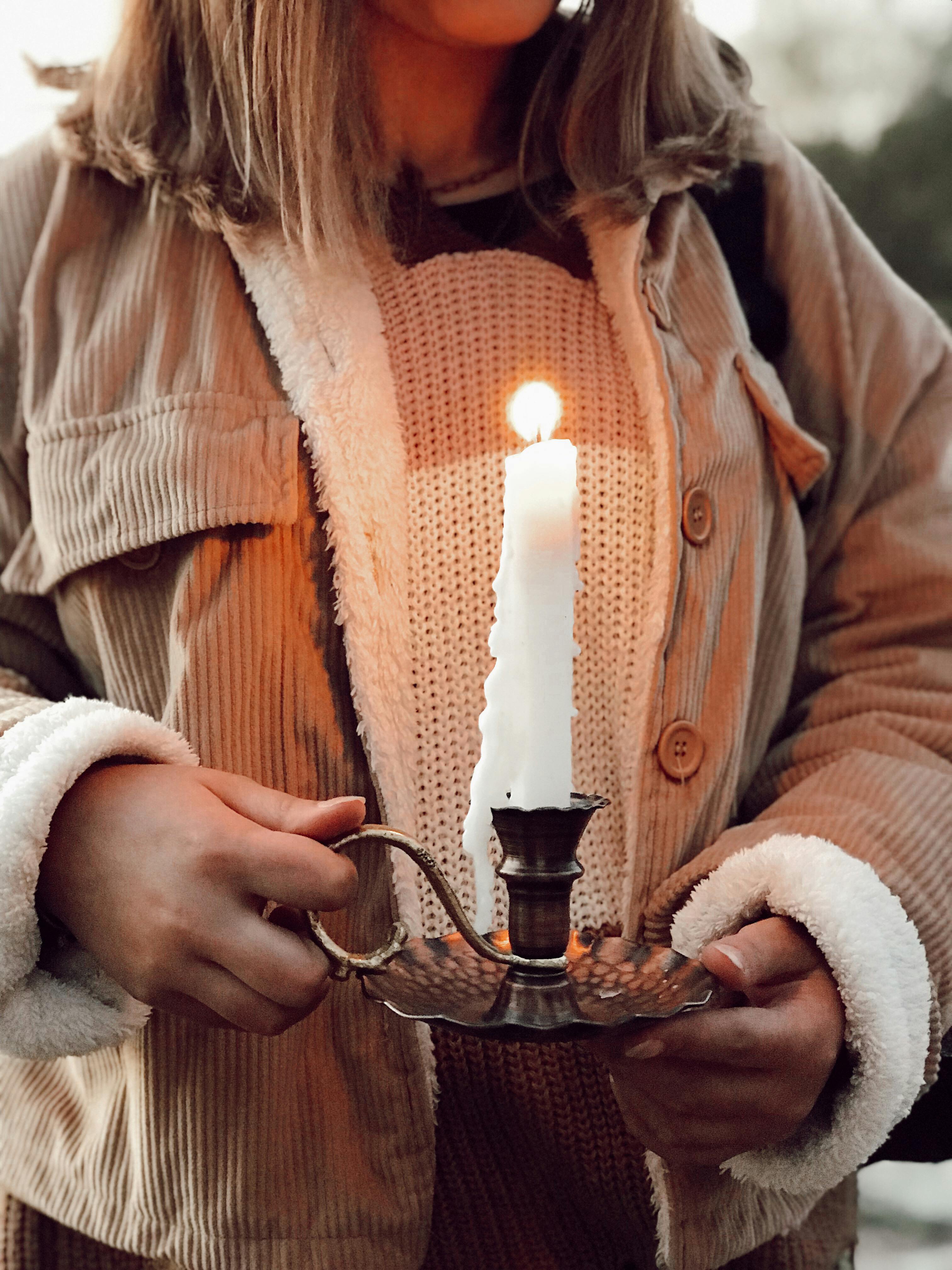 midsection of a woman holding a candlestick holder with a burning candle