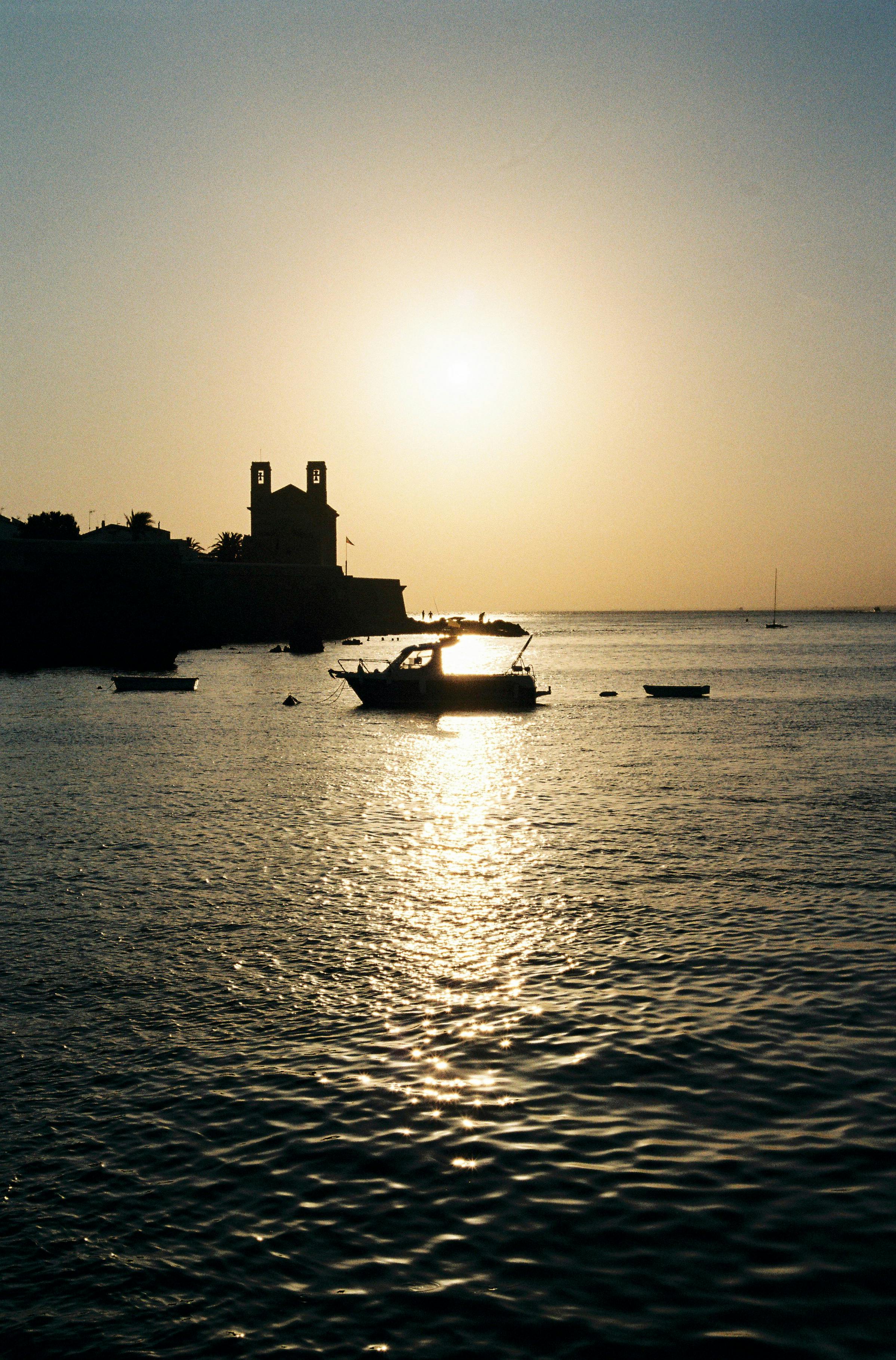 Silhouetted motorboat at sunset on tranquil coast with clear sky.