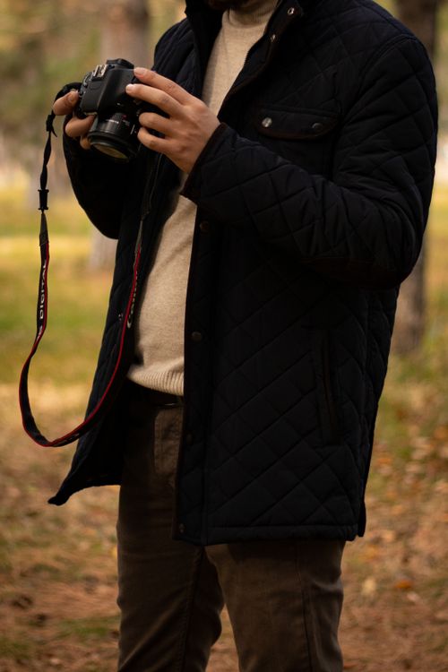 Free Close-up of a person holding a camera in a black quilted jacket outdoors. Stock Photo