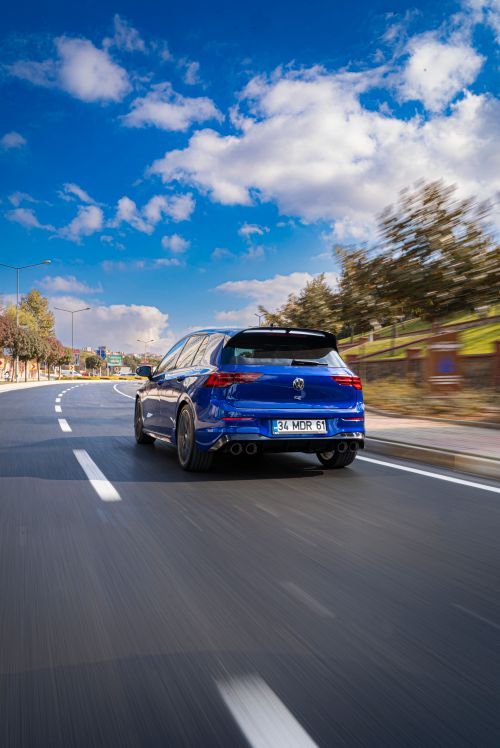 Free Dynamic shot of a blue hatchback car driving fast on a clear road with a sunny sky. Stock Photo