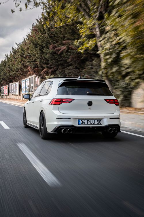 Free White hatchback car speeding down a deserted road lined with trees, capturing action and speed. Stock Photo