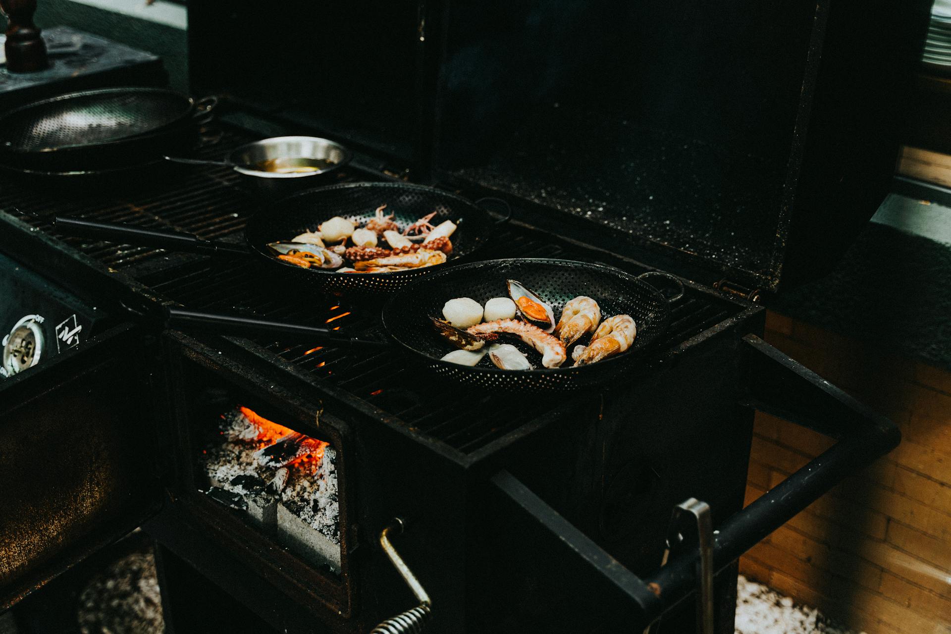 Delicious seafood including prawns and shellfish grilled on cast iron pans over an open flame grill.