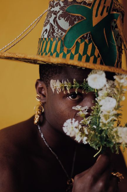 A captivating portrait of a man partially obscured by flowers, wearing a decorative hat, exuding cultural richness in Lagos, Nigeria.