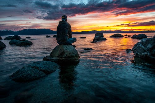 Ücretsiz Su Kütlesi üzerinde Kayanın üzerinde Oturan Kişi Stok Fotoğraflar