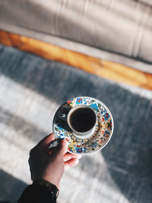 Free A hand holds a beautifully ornate coffee cup indoors with sunlight casting elegant shadows. Stock Photo