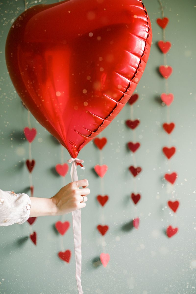 Person holding a heart-shaped balloon against a background of heart paper cutouts