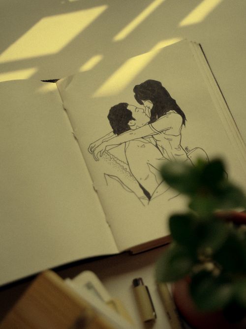 Free Warm sunlight casts over a hand-drawn sketch of a couple embracing in an open notebook. Stock Photo