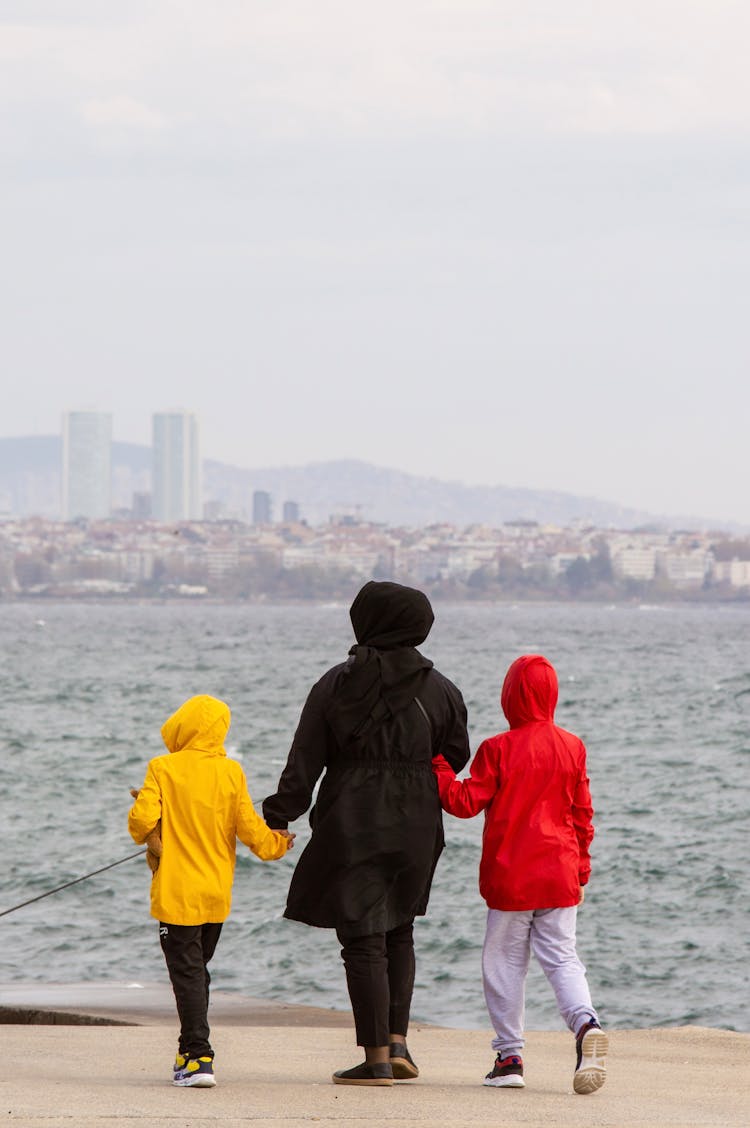 A Person In Black Hoodie Walking With Kids Near The Ocean