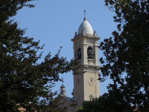 Free Beautiful architectural bell tower framed by green trees under a clear blue sky. Stock Photo