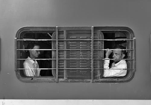 View of Two Men Sitting by a Window in a Train Photographed from the Outside 