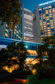 Illuminated modern skyscrapers towering over lush greenery at night, creating a compelling urban scene.