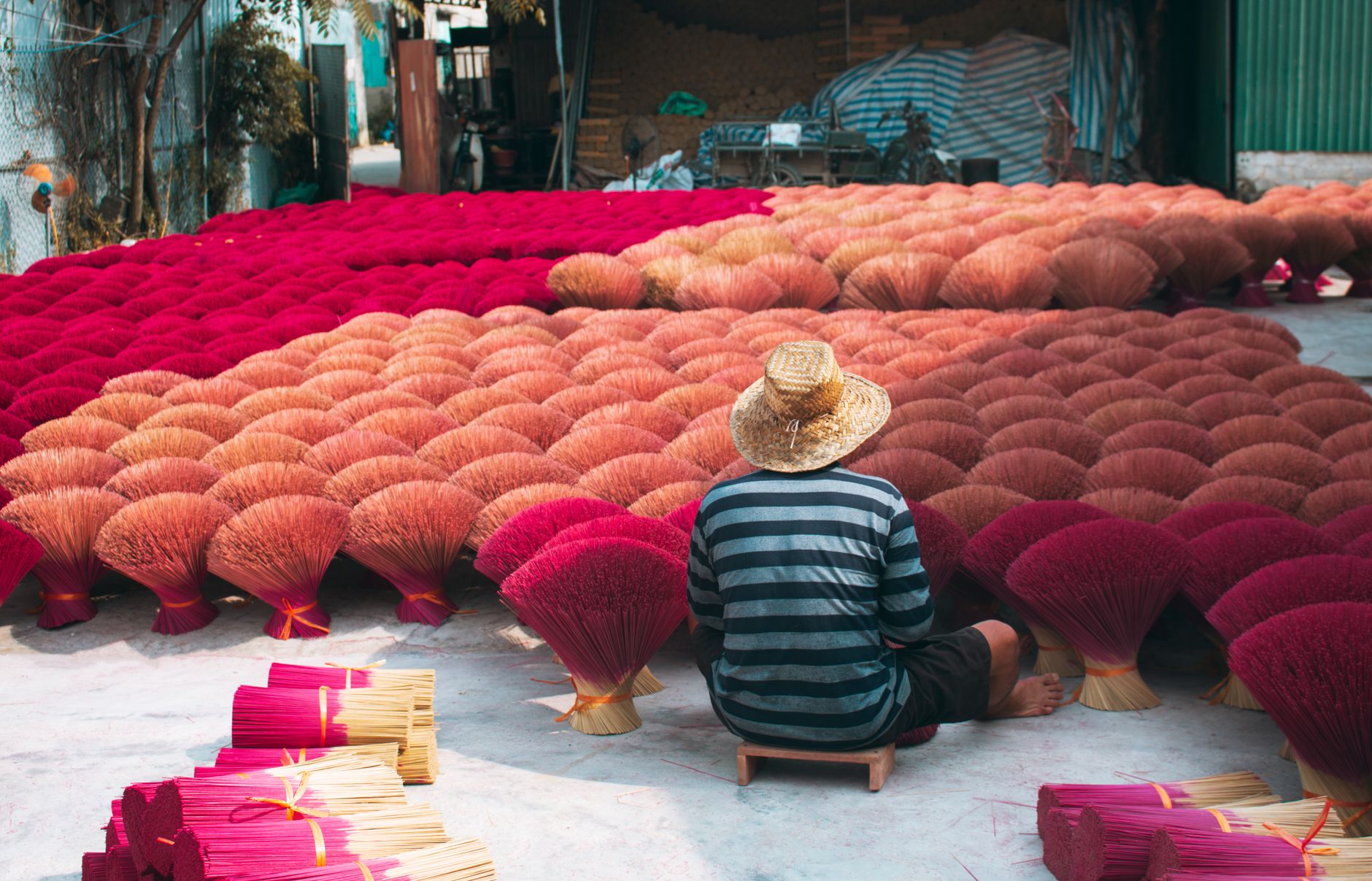 Laborer sits among vibrant incense sticks in Hanoi, showcasing Vietnamese tradition.