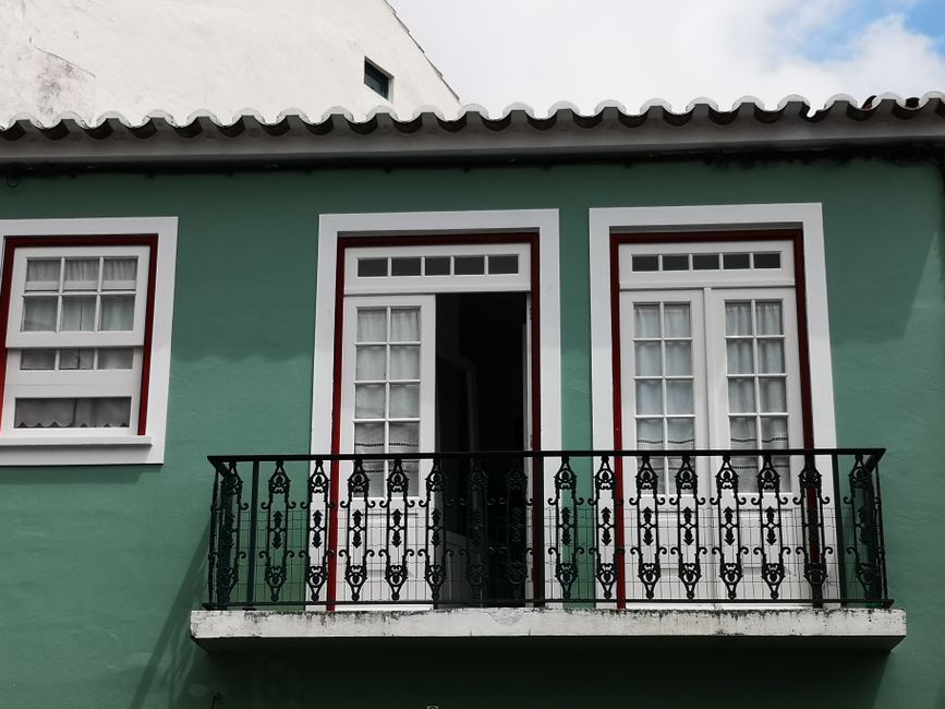 Green building with a classic iron balcony and white windows, capturing architectural details.