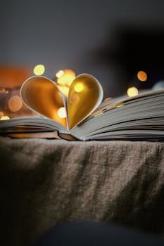 Open book with pages folded into a heart shape, surrounded by warm bokeh lights.