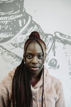 Close-up of a stylish African American woman with braids in front of artistic mural.