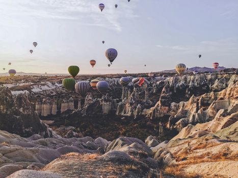 Colorful hot air balloons soar above the rocky valleys of Cappadocia at sunrise, Turkey.
