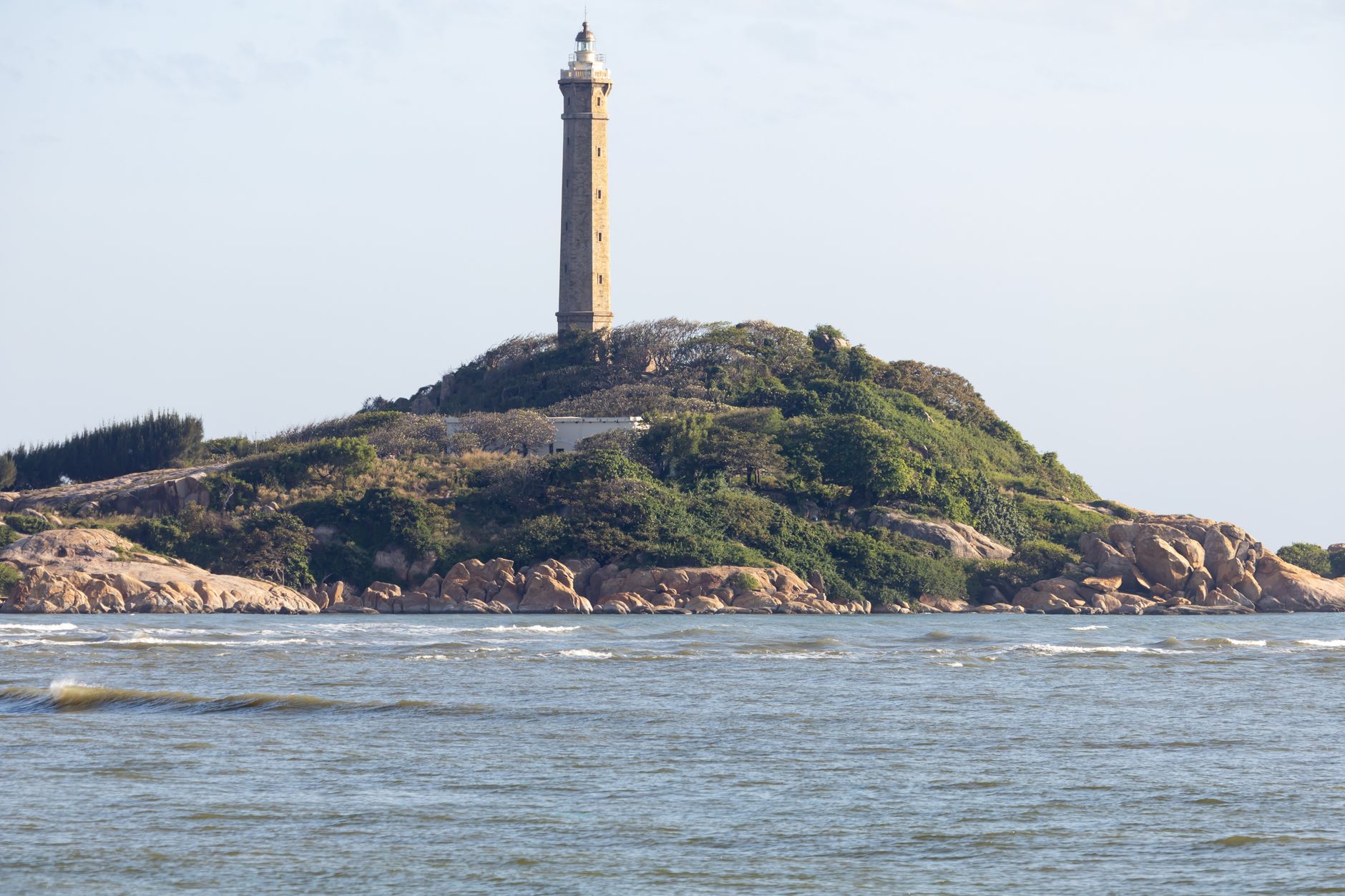 A lighthouse stands tall on a lush, rocky island surrounded by the serene ocean.
