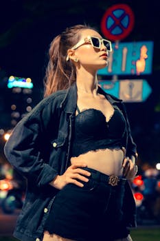 Confident woman in black outfit and sunglasses posing outdoors at night.