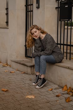 Casually dressed young woman with long blonde hair sitting on an urban sidewalk.