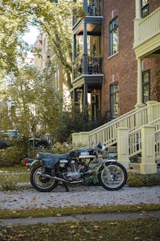 Classic black motorcycle parked outside townhouses in a leafy Québec street, capturing a nostalgic vibe.