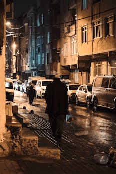 A dimly lit urban street with wet pavement and pedestrians braving the night.