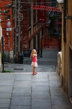 A child standing on a street in Genova, Italy, wearing a red tank top and pink skirt.