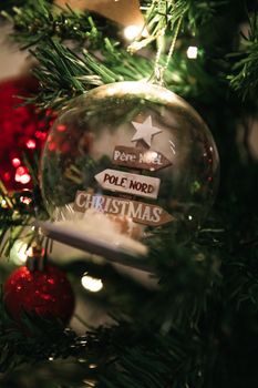 A close-up view of a Christmas ornament on a decorated tree branch, featuring festive text.