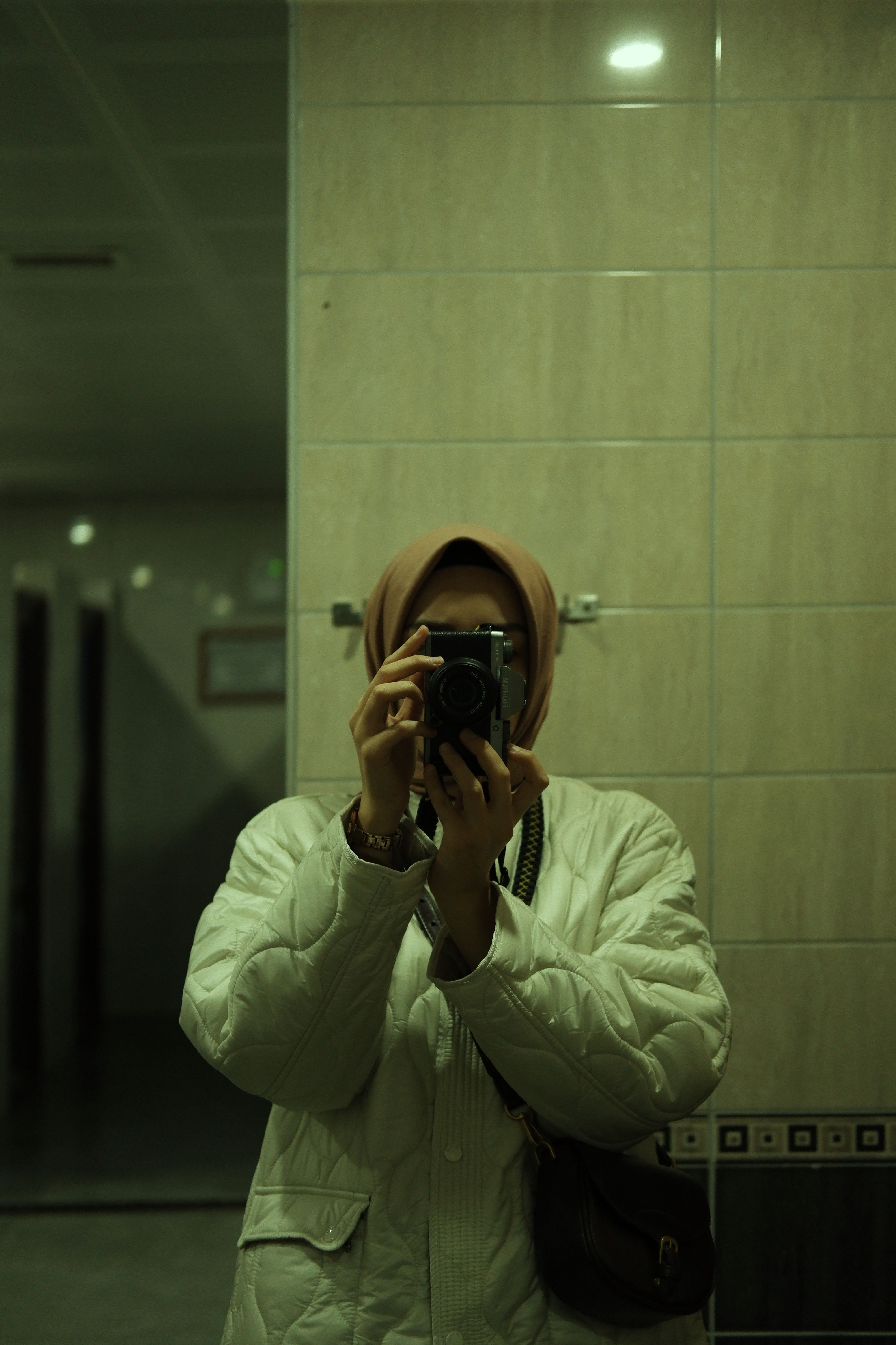 A person in a white jacket takes a mirror selfie indoors.