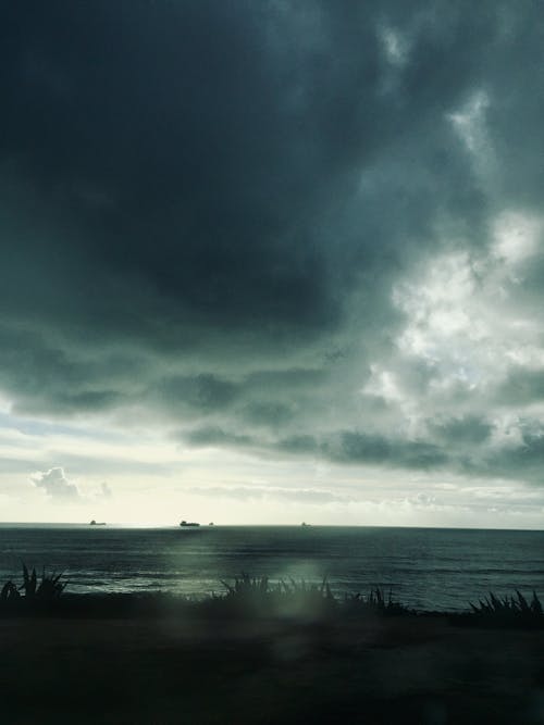 Free stock photo of calm sea, cargo ships, dark clouds