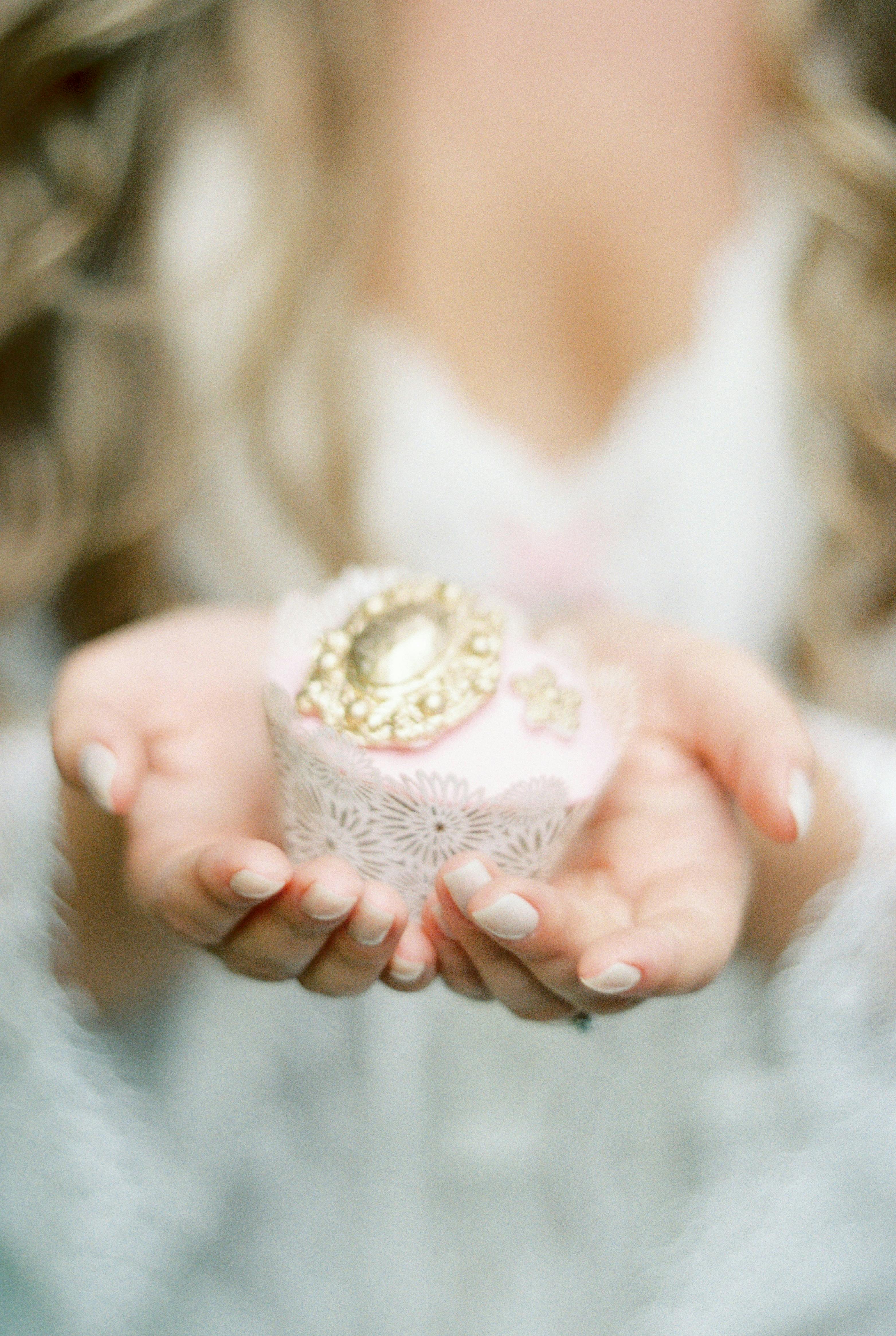 Close-up of a beautifully decorated cupcake held gently by a bride.