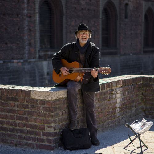 Free Smiling street musician playing guitar on brick wall with urban backdrop. Stock Photo