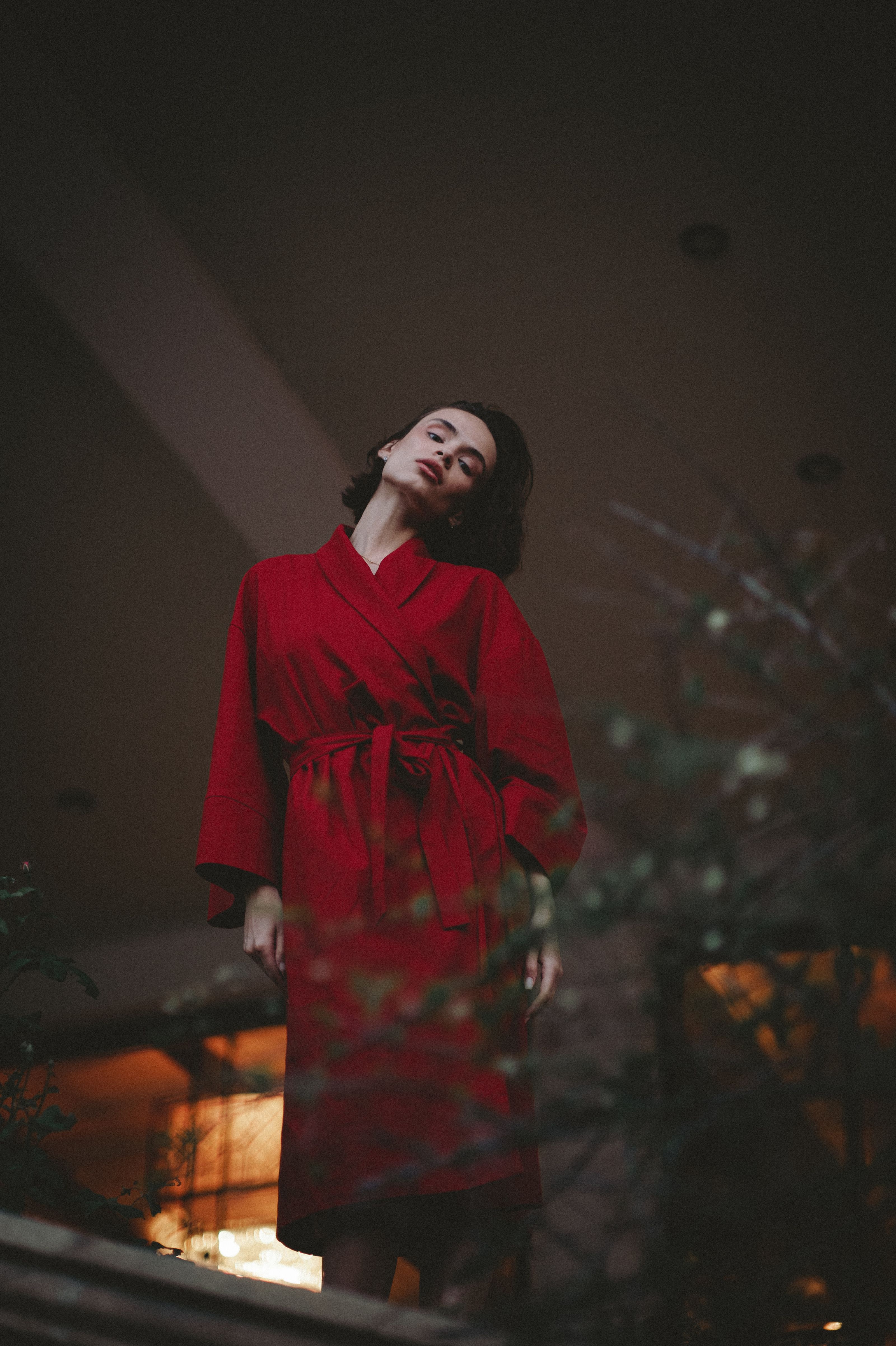 Mulher estilosa em um robe vermelho posando elegantemente em um ambiente interno com iluminação suave.