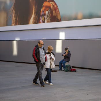 A street musician plays violin as a couple walks by on a city sidewalk.