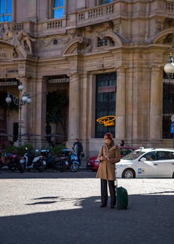A woman stands with luggage on a sunny urban street, surrounded by historic architecture.